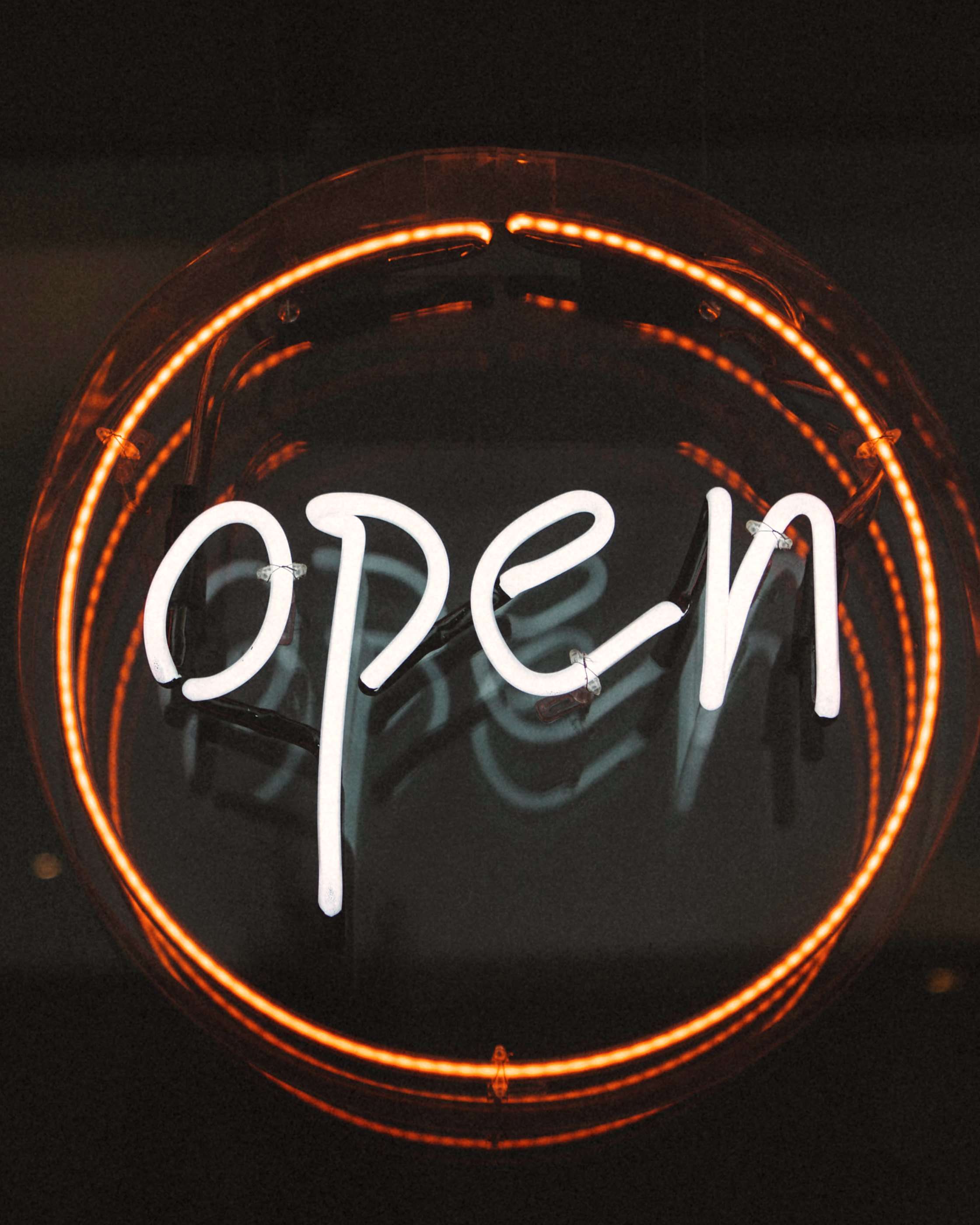 A round neon sign reading "open" glowing in a dark shop window