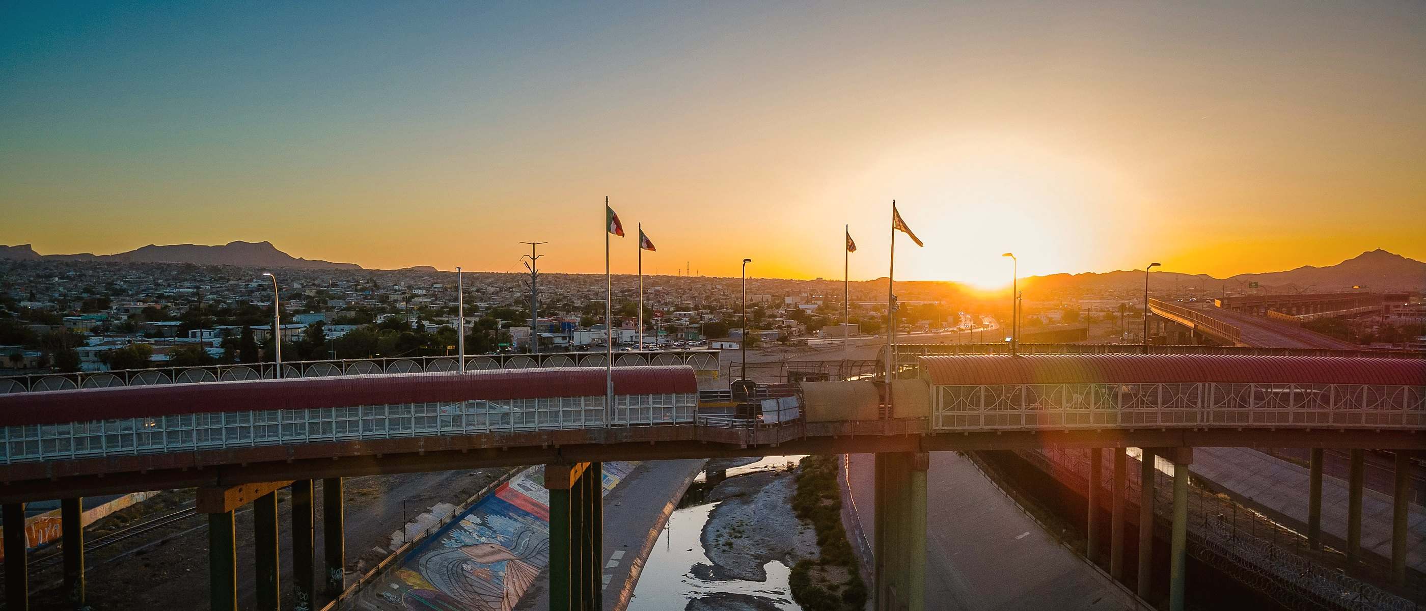 Sunset over an international bridge and the Rio Grande channel between El Paso and Ciudad Juárez, flags on the far bank