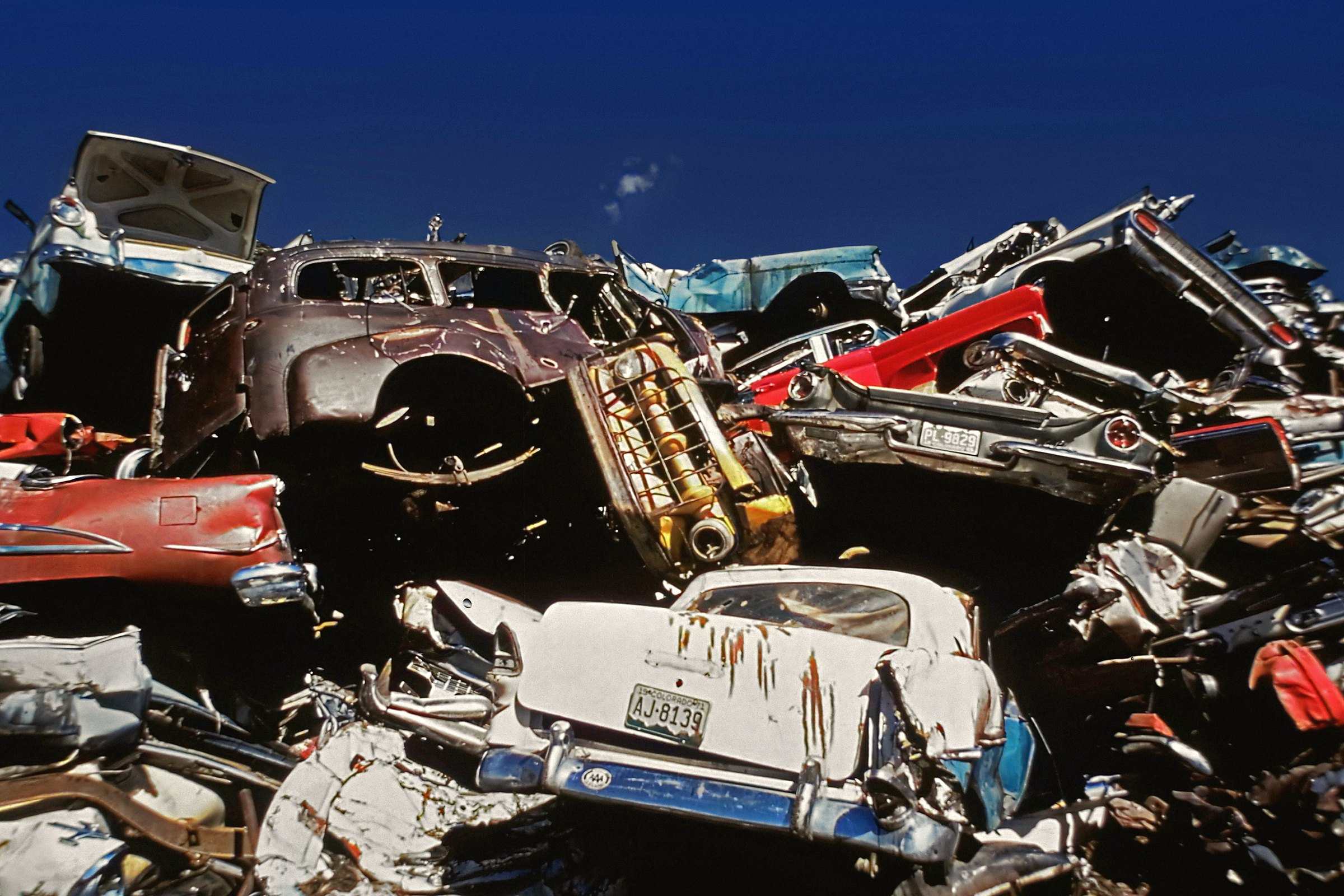 Crushed and stacked cars in a scrapyard under a deep blue sky