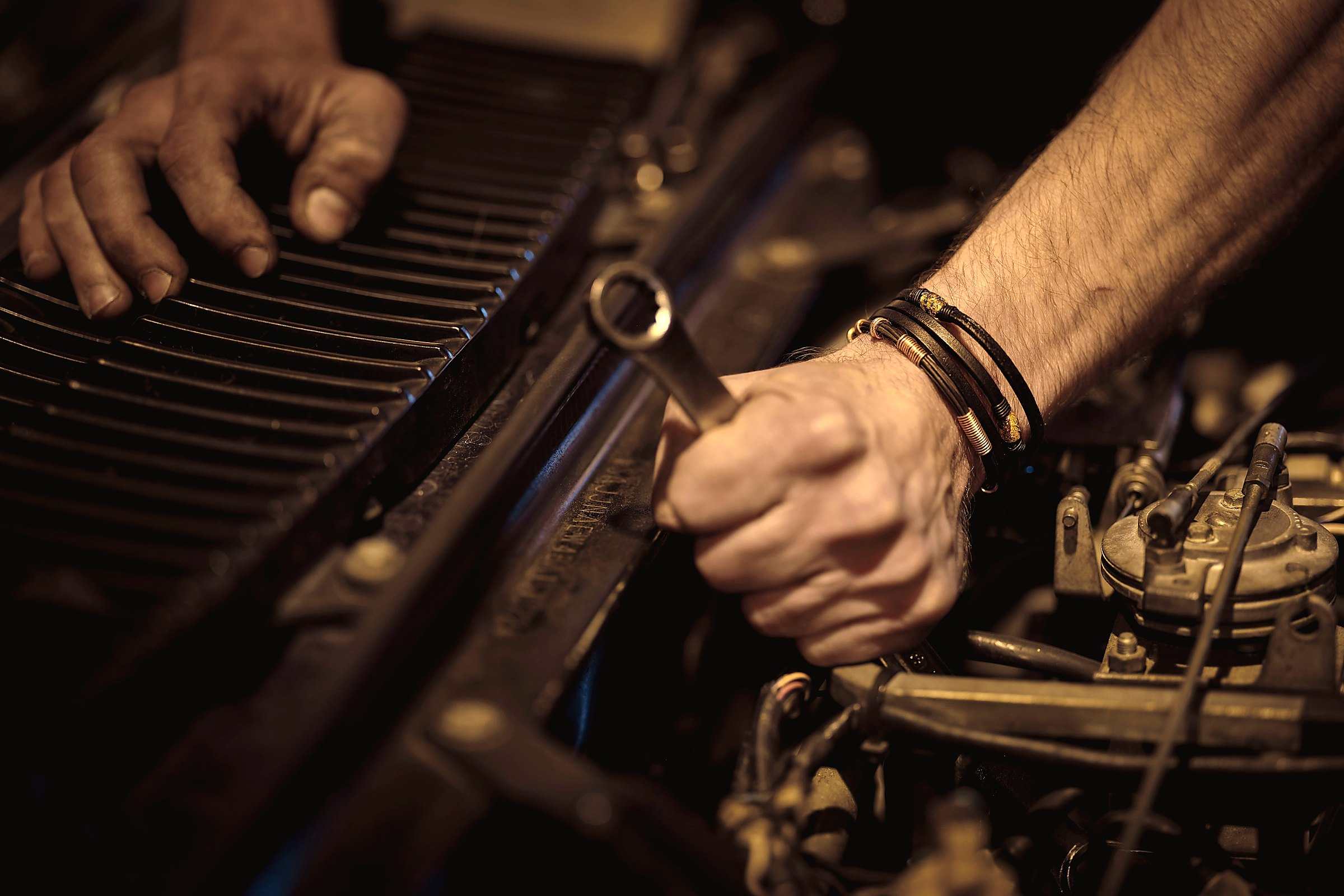 Greasy hands working a wrench on a car engine