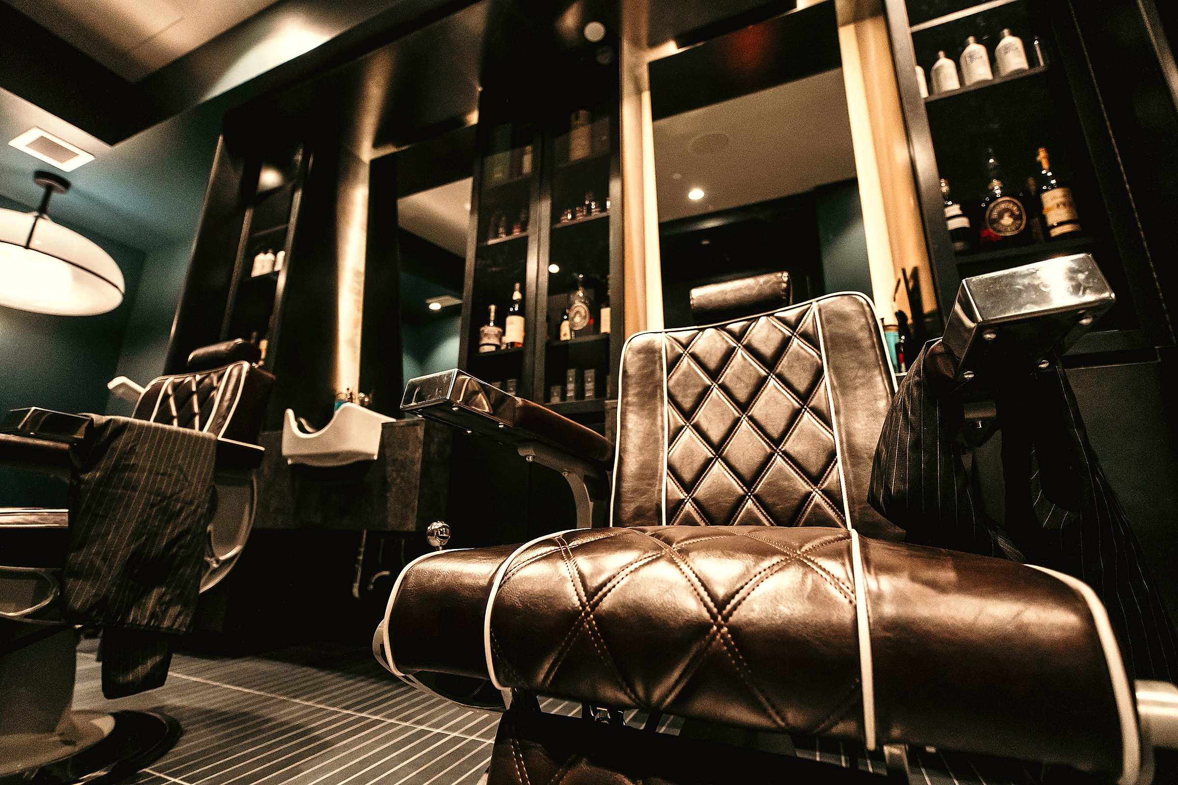 A tufted leather barber chair facing the mirror in a dimly lit barbershop