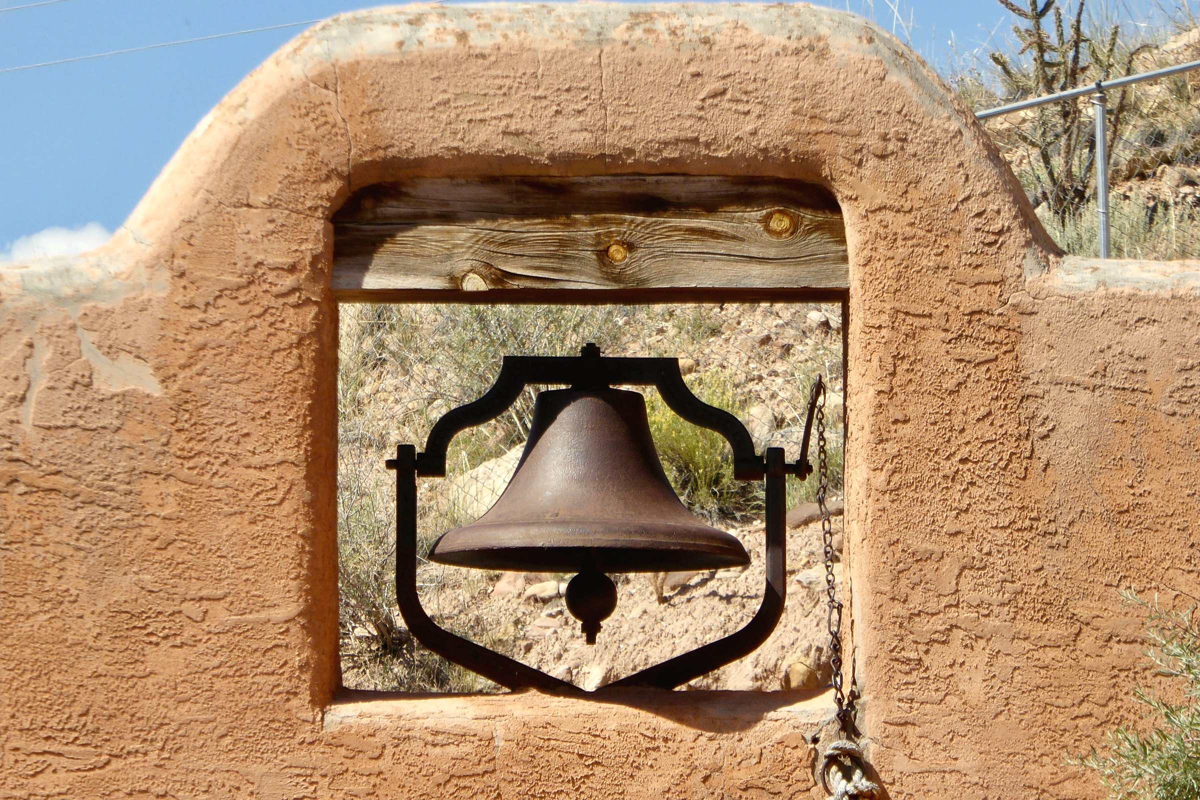 An iron bell hanging in an arched opening in an adobe wall