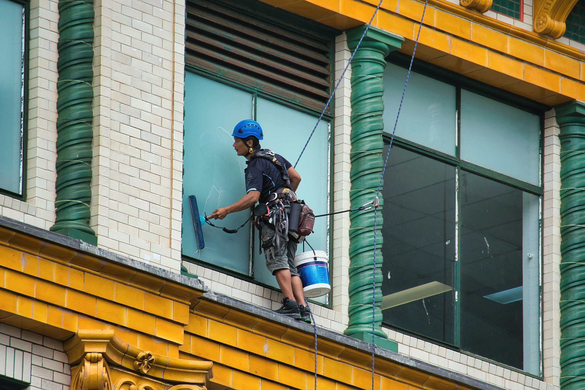 A window cleaner on ropes washing the windows of a yellow and green building