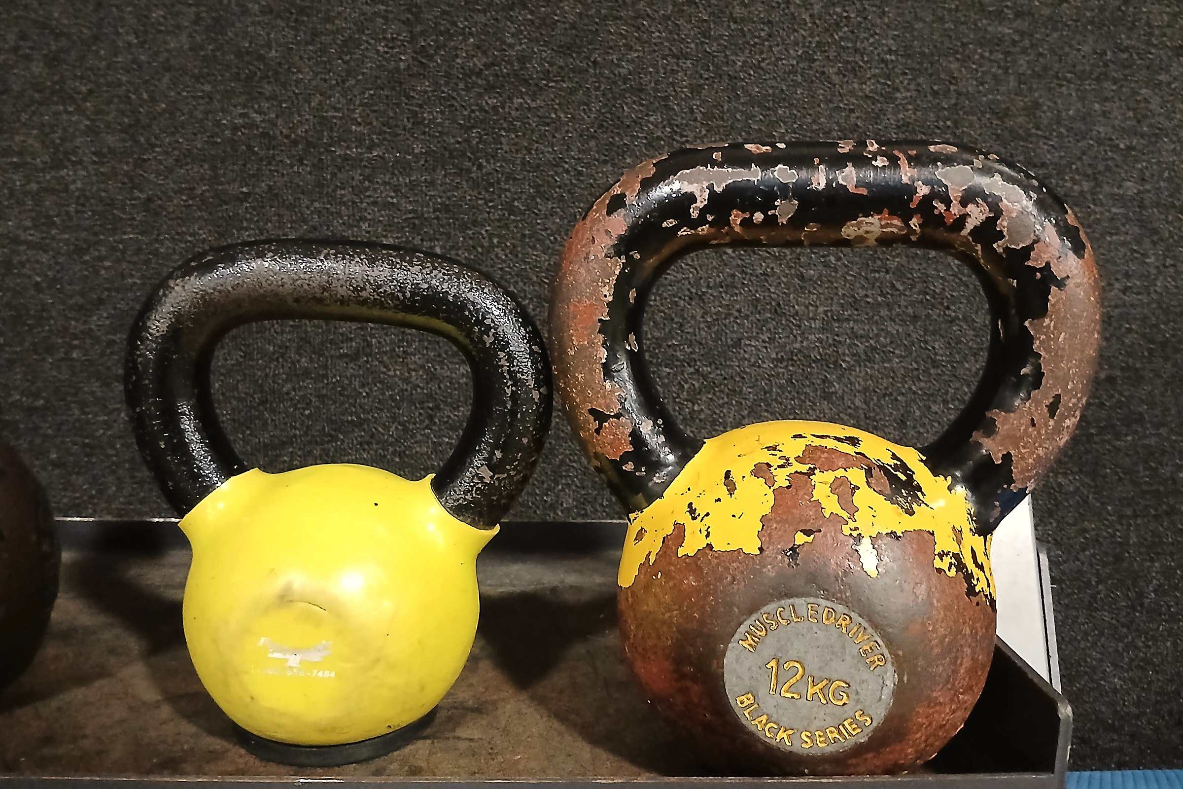 Two worn kettlebells, one yellow and one rusty, on a gym shelf
