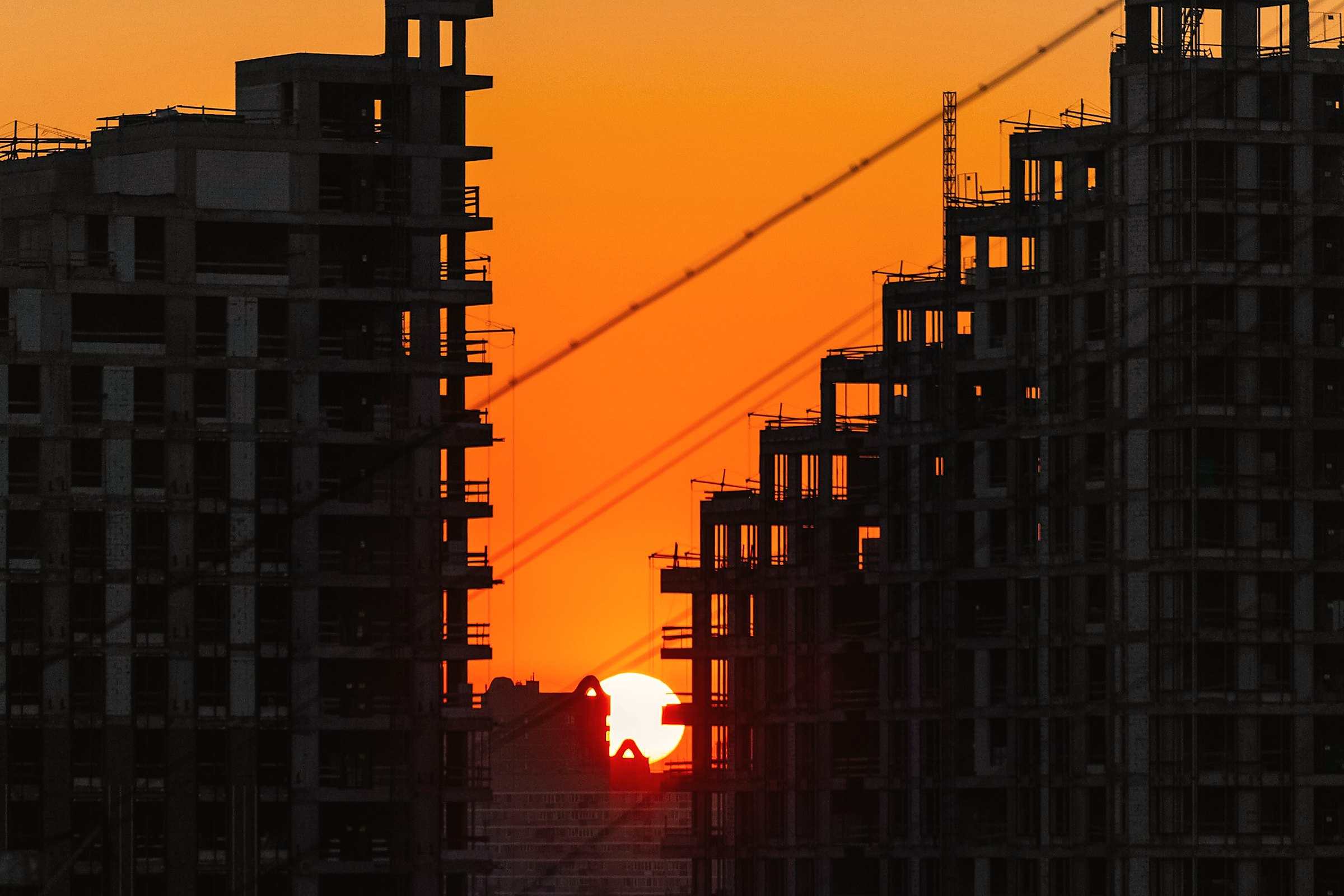 Buildings under construction silhouetted against an orange sunset