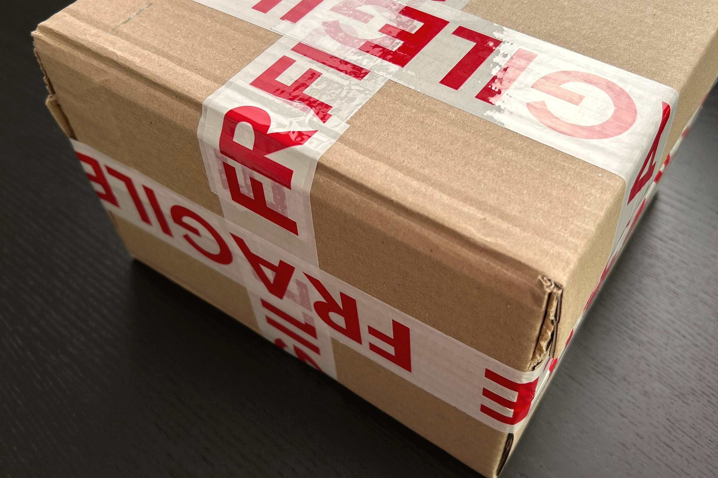 A cardboard shipping box sealed with red FRAGILE tape