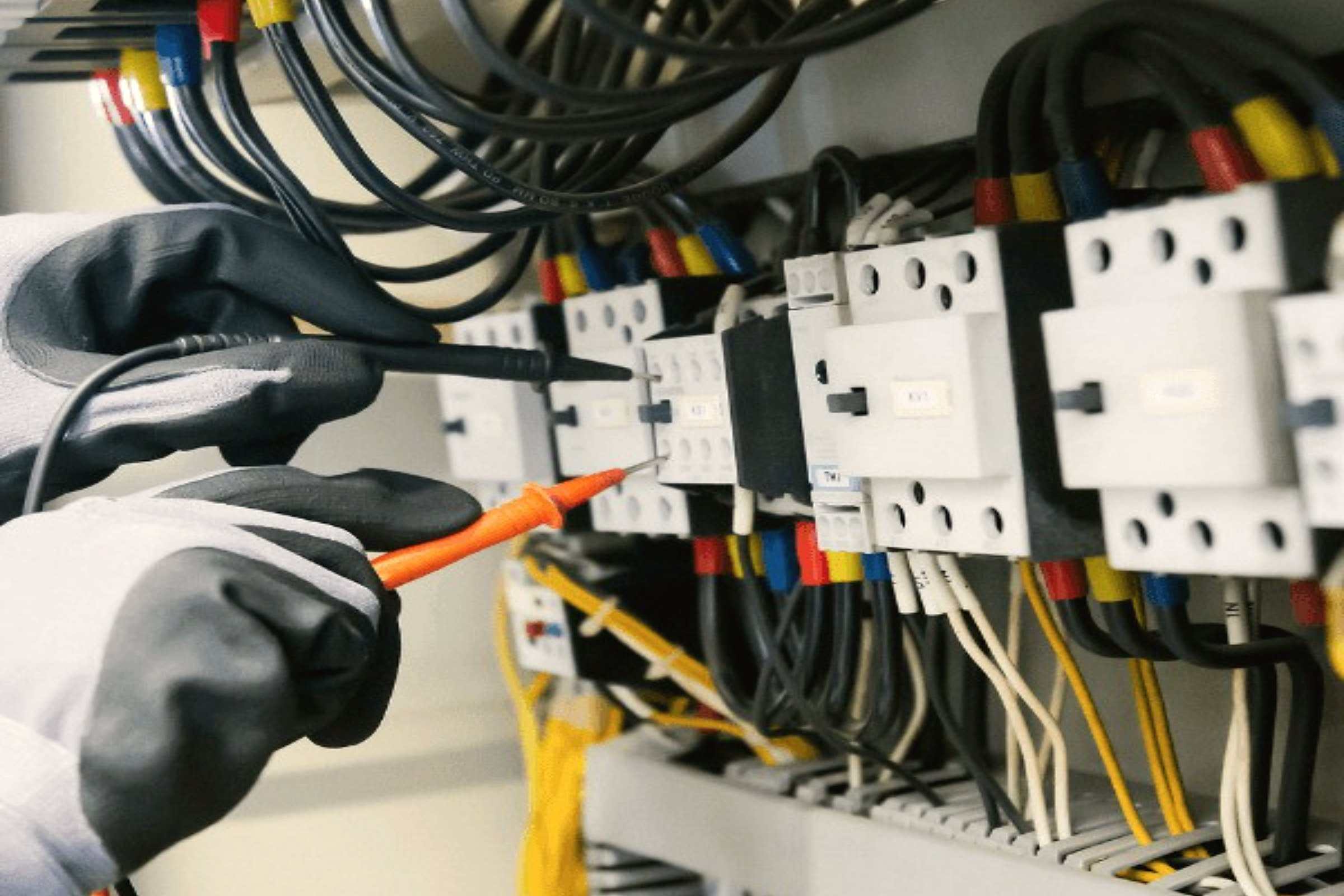 Gloved hands testing the wiring of an electrical control panel