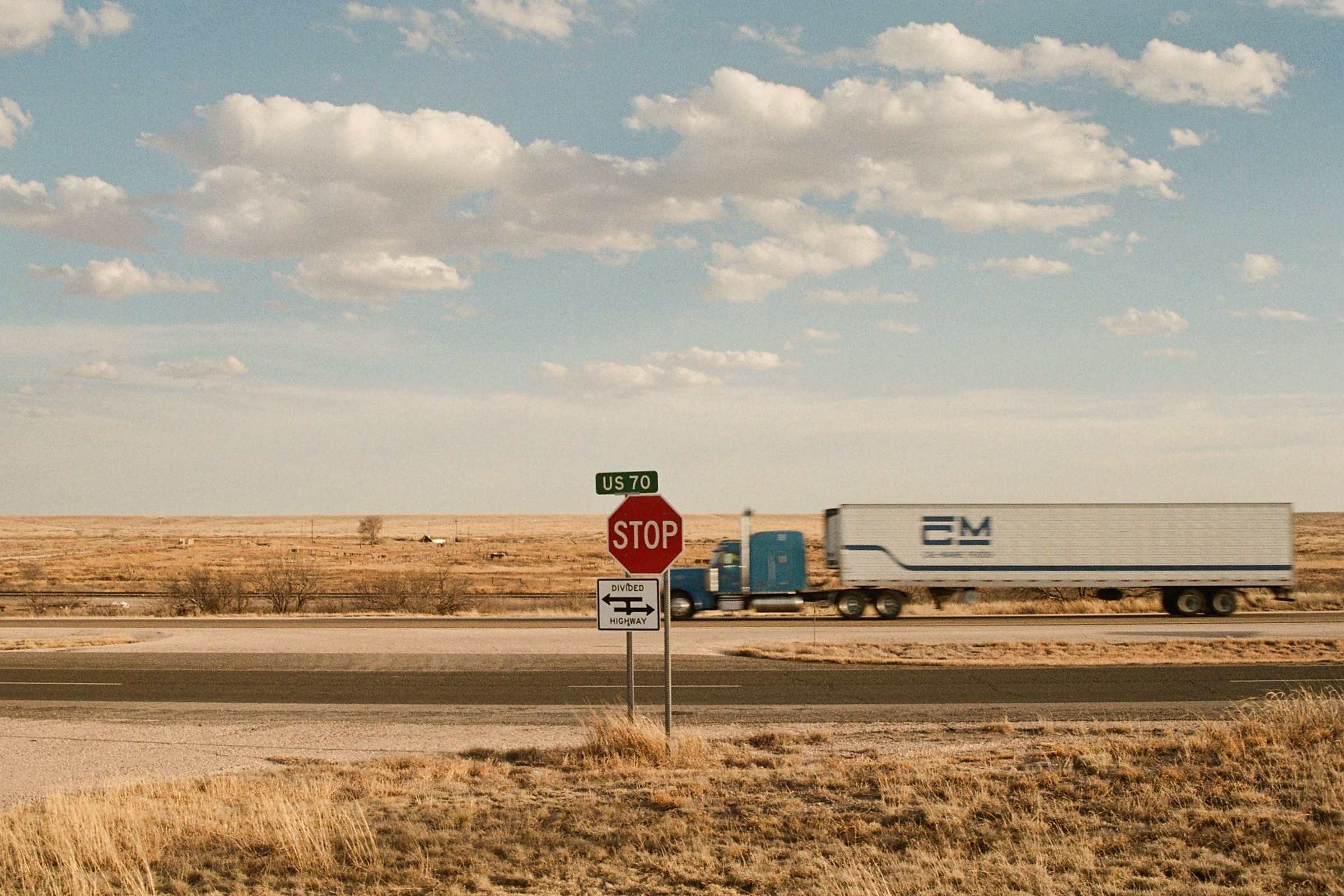 A semi-truck on US 70 crossing the open desert grassland of New Mexico, past a stop sign
