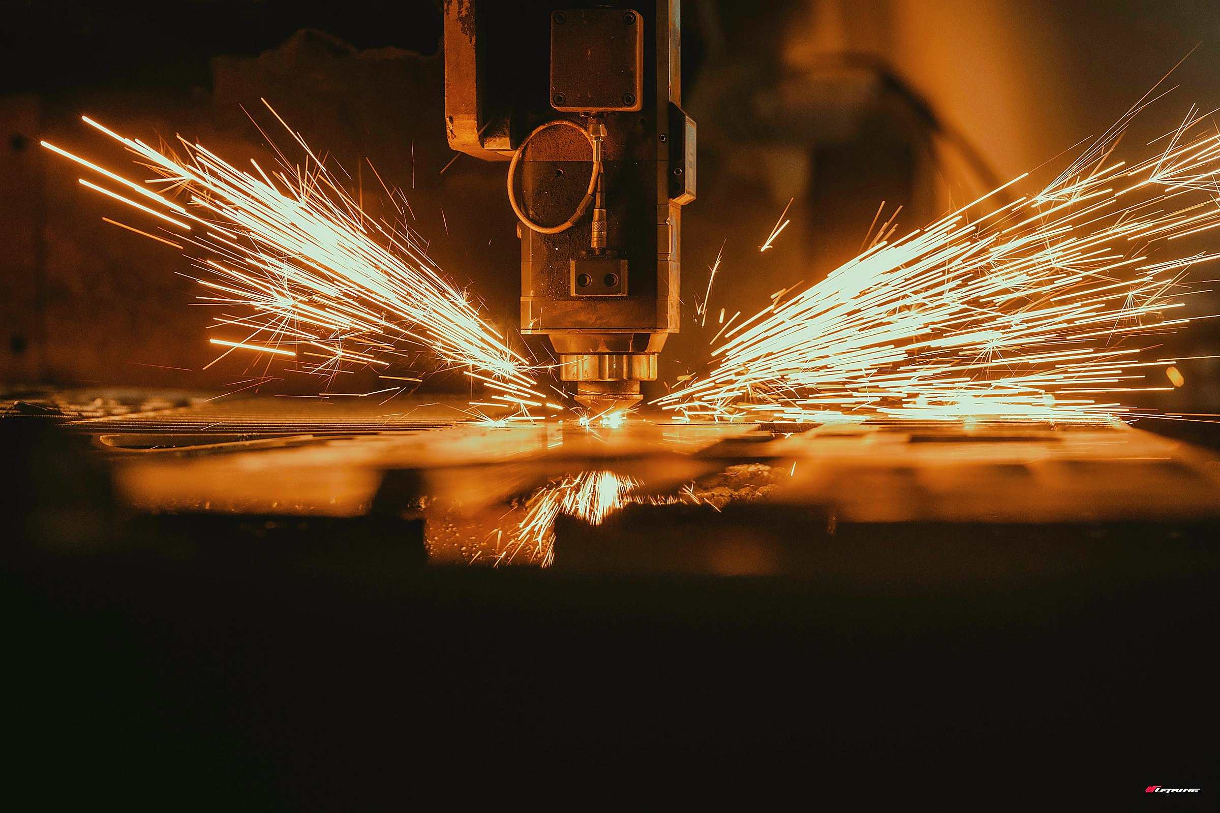 Sparks fanning out from a CNC cutting machine in a dark workshop