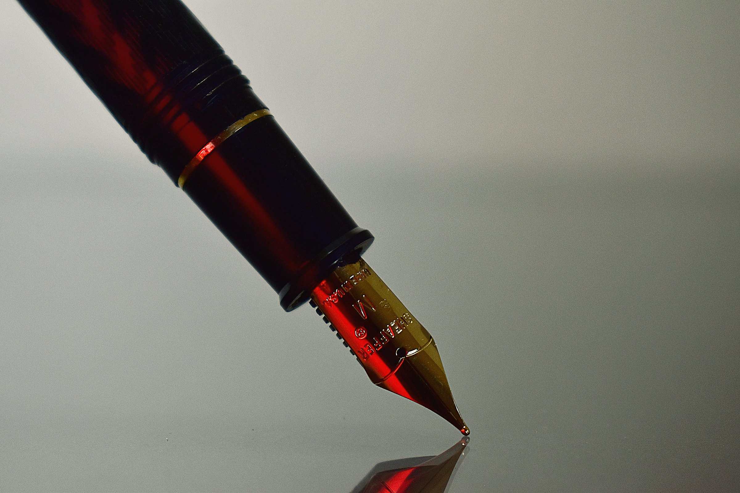 The gold nib of a red fountain pen touching paper