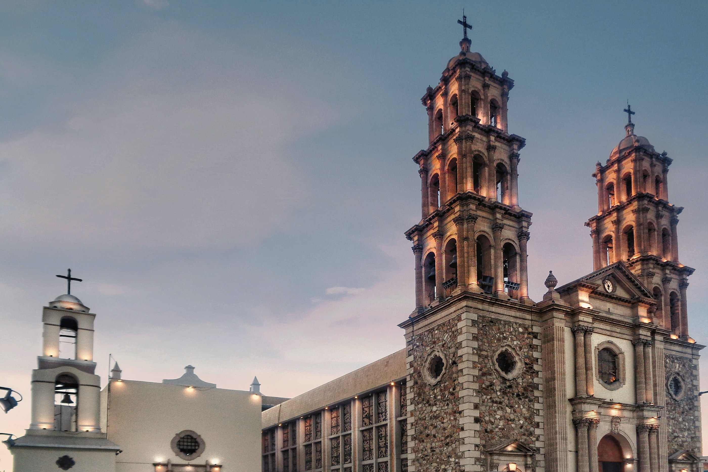 The twin towers of the Ciudad Juárez cathedral lit at dusk, with the white Misión de Guadalupe beside them
