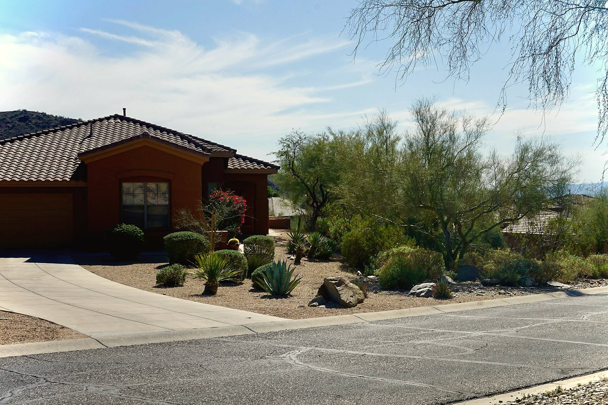 A stucco house with a tile roof, desert landscaping and a driveway under a clear sky