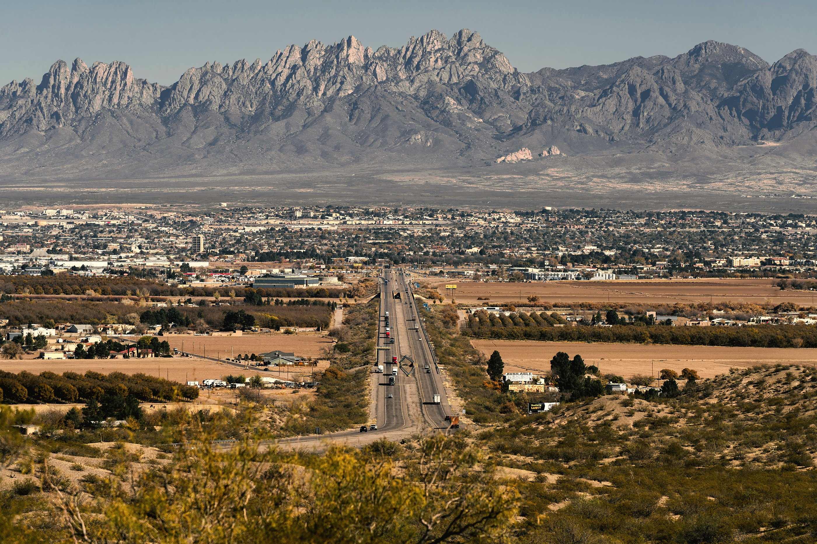 Las Cruces seen from the west mesa, a straight road running toward the full crest of the Organ Mountains