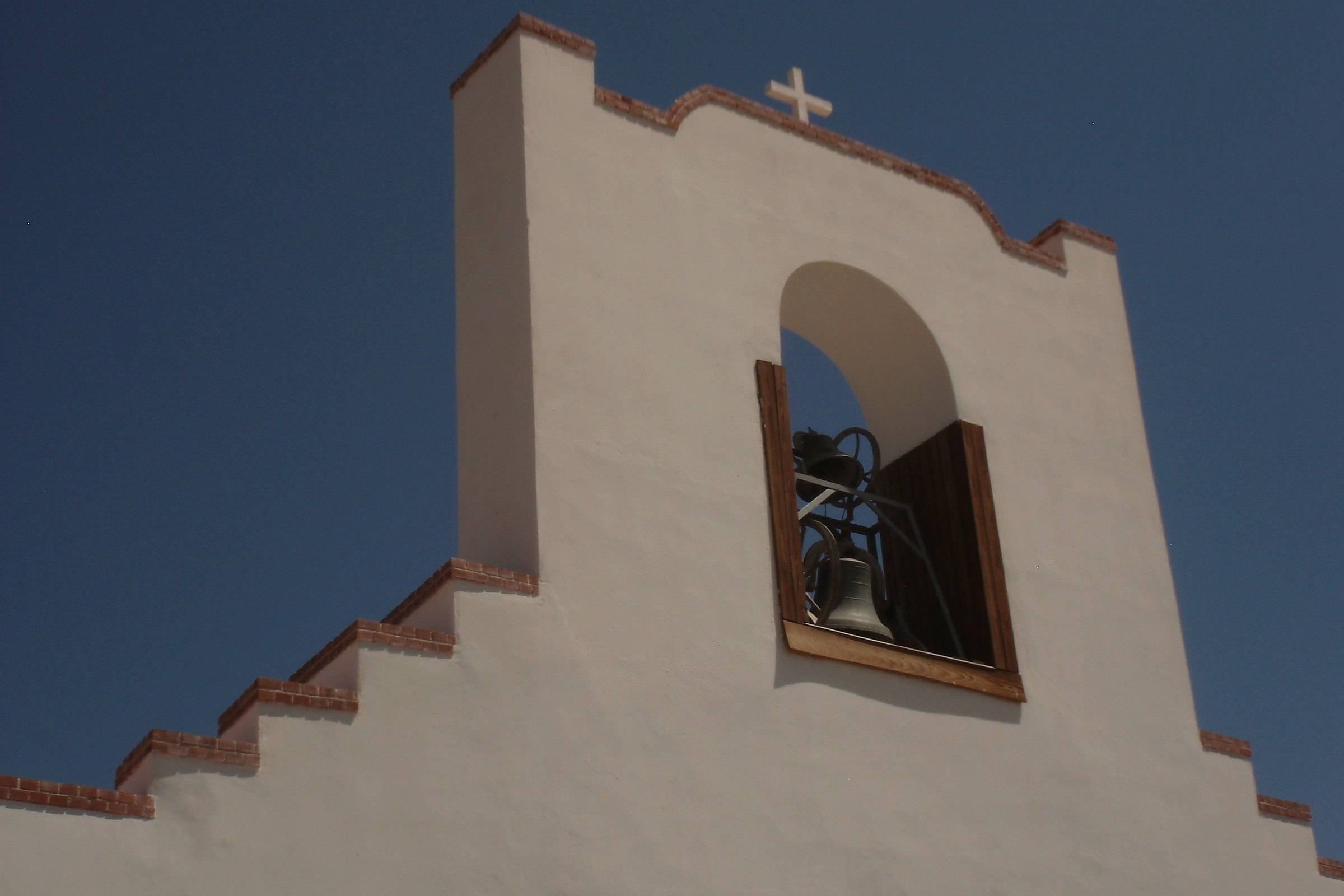 The bell in its arched gable above the stepped white parapet of the Socorro Mission