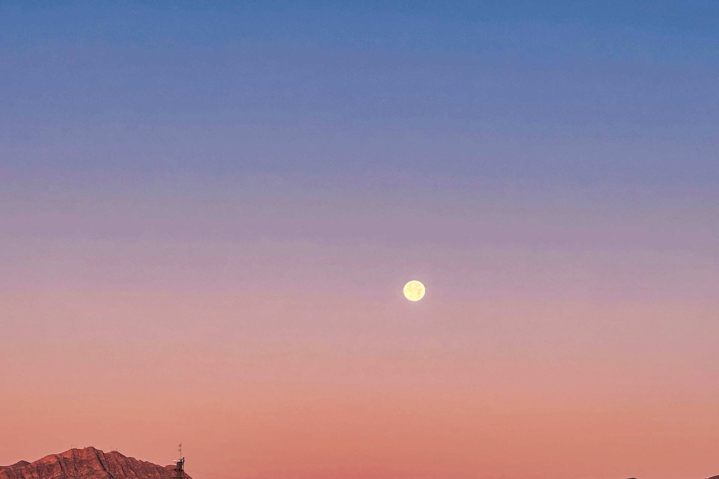 The west face of the Franklin Mountains in El Paso glowing pink at dusk under a rising full moon