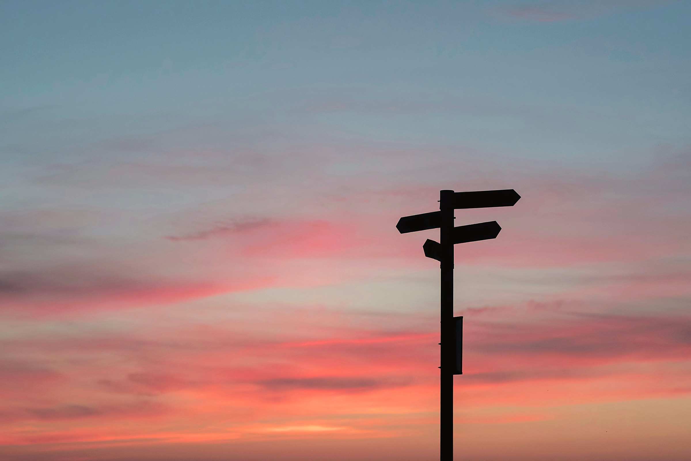 A signpost silhouetted against a pink and orange sunset sky