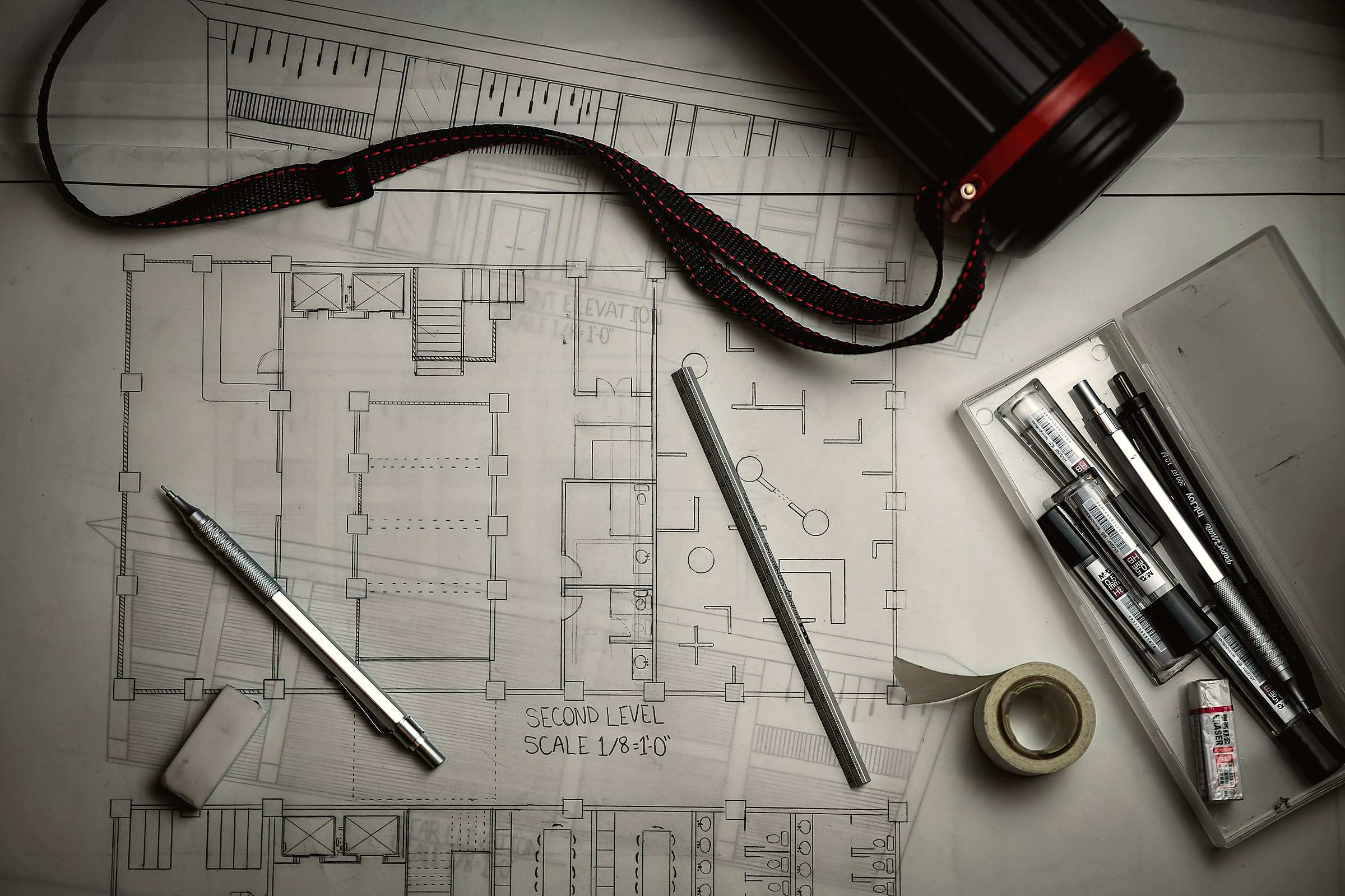 Architectural blueprints with drafting pencils, a metal ruler and tape