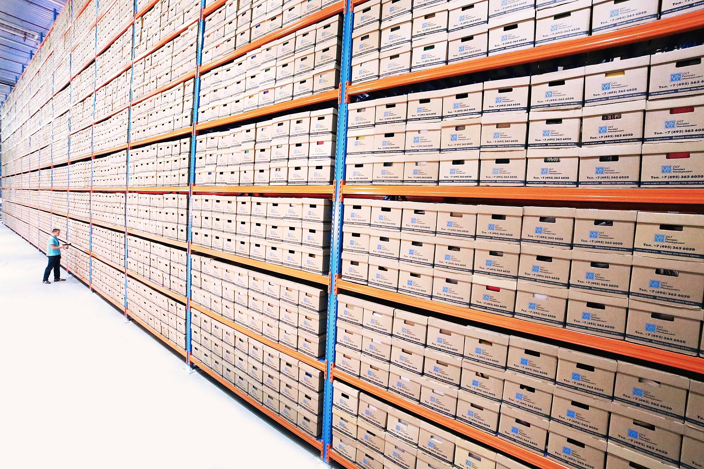 Long rows of labelled archive boxes on tall shelves, a lone person at the far end