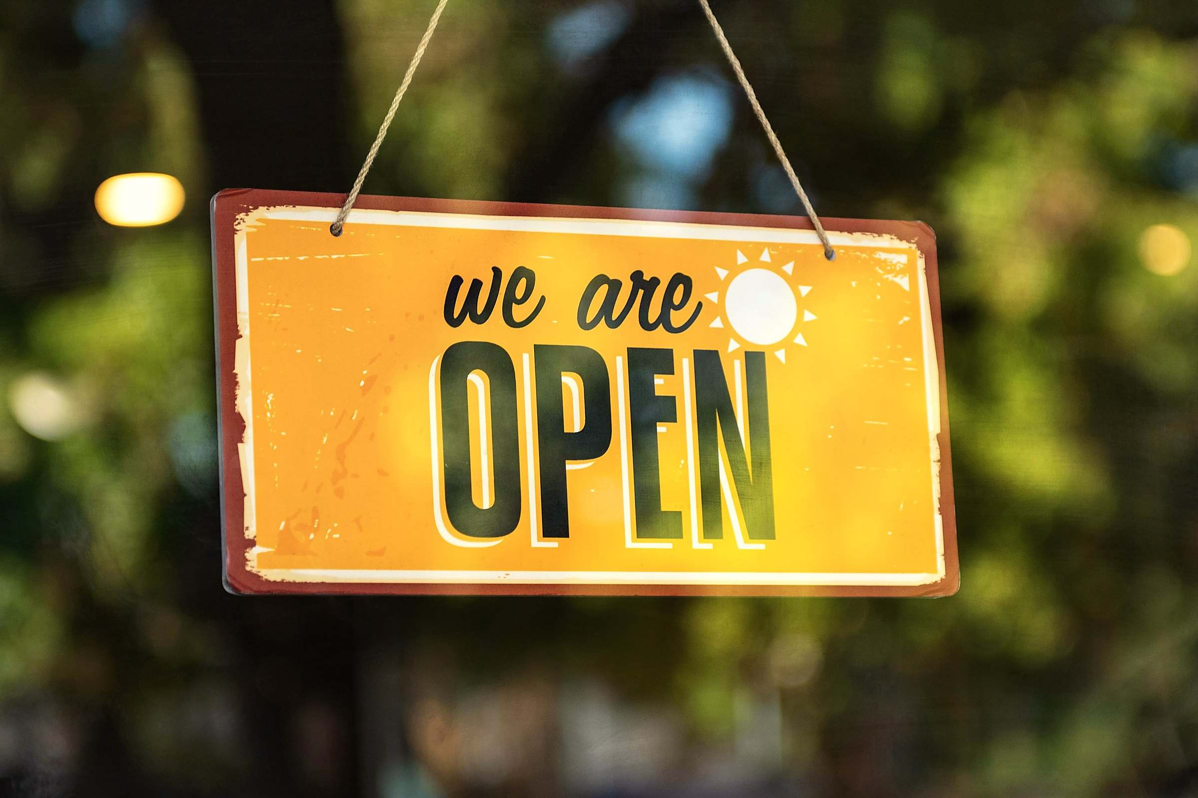 A yellow "we are open" sign hanging in a shop window