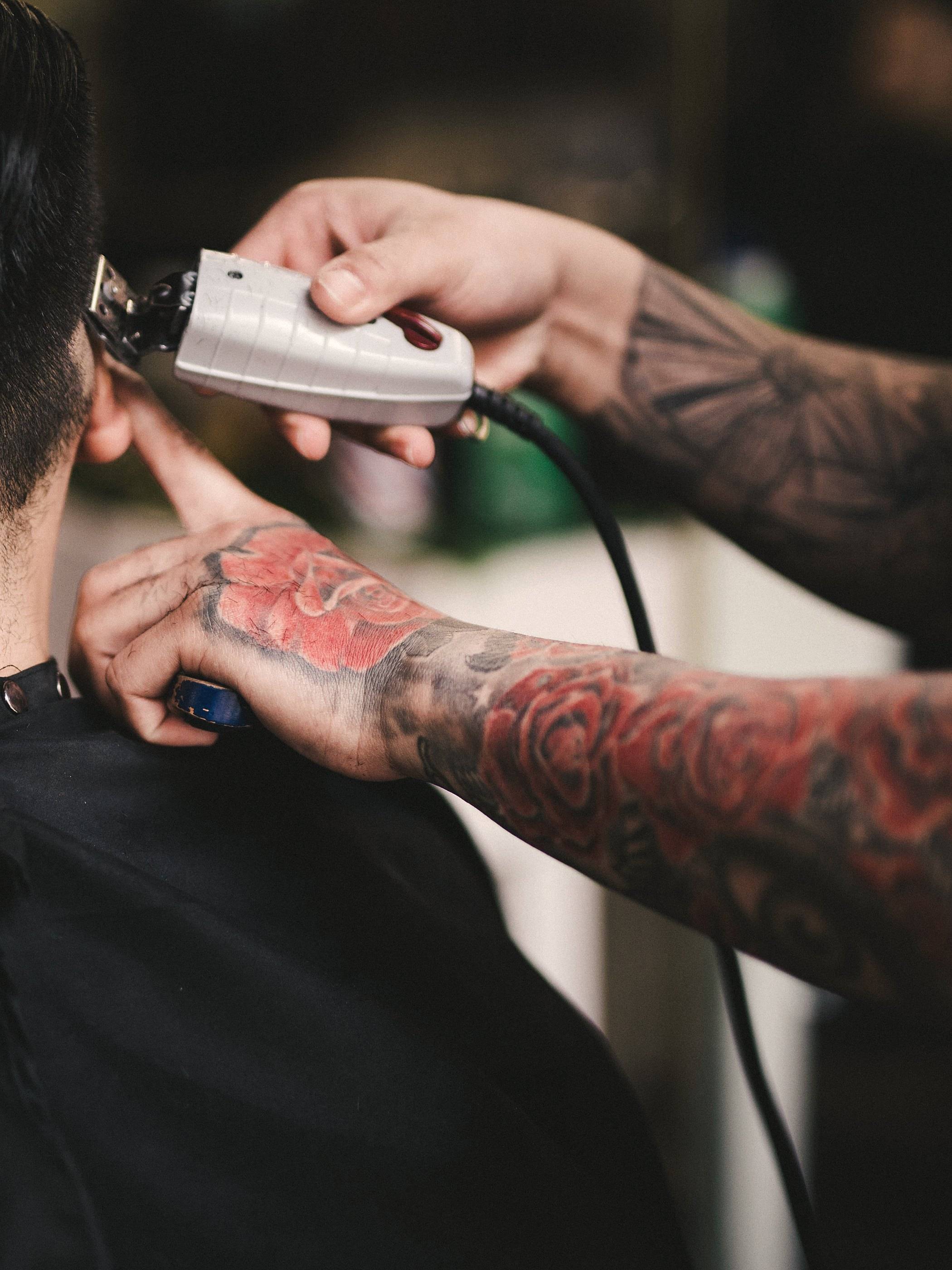A barber's tattooed hands trimming the back of a client's head with clippers