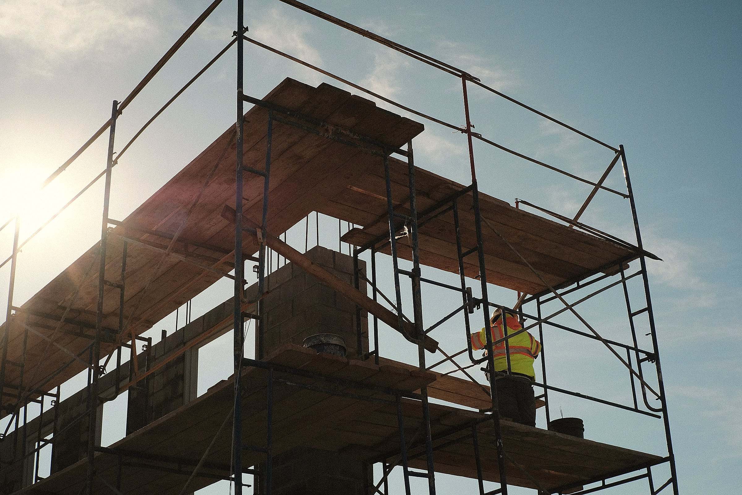 A worker on a steel scaffold, backlit by the sun